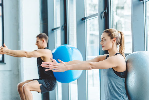 young man and woman exercising on fitness balls in gym - Fotó, kép
