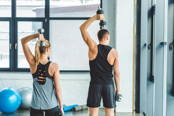back view of couple in sportswear training with dumbbells in gym - Fotó, kép