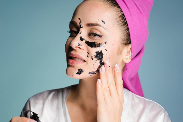 a young girl with a pink towel on her head removes from her face a black mask against acne - Fotó, kép