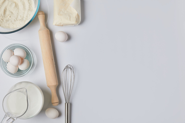 top view of eggs, milk and rolling pin on white tabletop - Photo, image