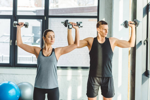 focused young man and woman exercising with dumbbells in gym - Foto, Imagem