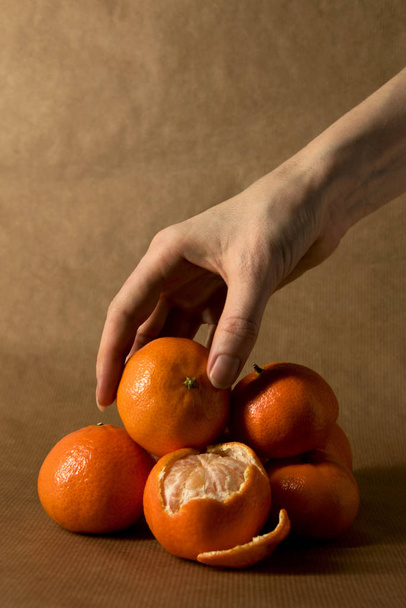 Een vrouwelijke hand te grijpen van een stapel van clementines op bruin papier - Foto, afbeelding