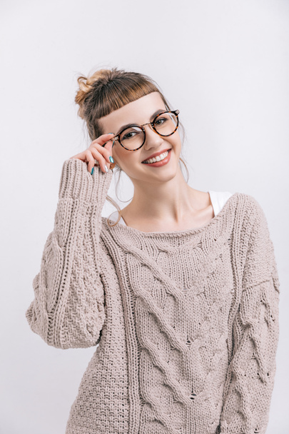 sonriente chica de pie y tocando gafas aisladas en blanco
 - Foto, Imagen