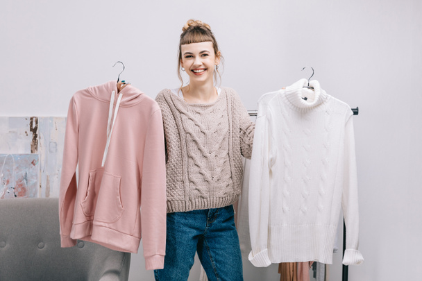 smiling girl standing and holding hangers with sweaters - Fotoğraf, Görsel