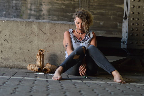 una mujer punk desesperada bajo un puente con botellas de alcohol y otras drogas a su alrededor
  - Foto, Imagen