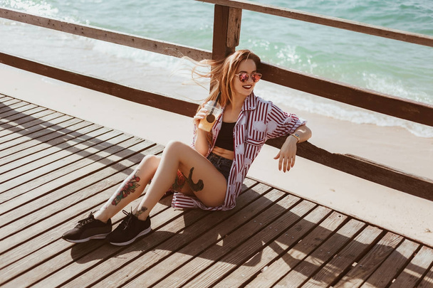 young woman with plastic cup sitting on wooden pier at beach - Foto, Imagem