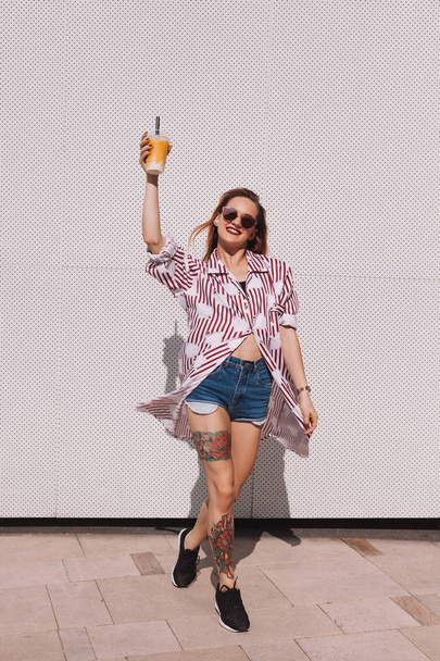 smiling woman holding plastic cup of cocktail in front of white wall - Foto, Bild