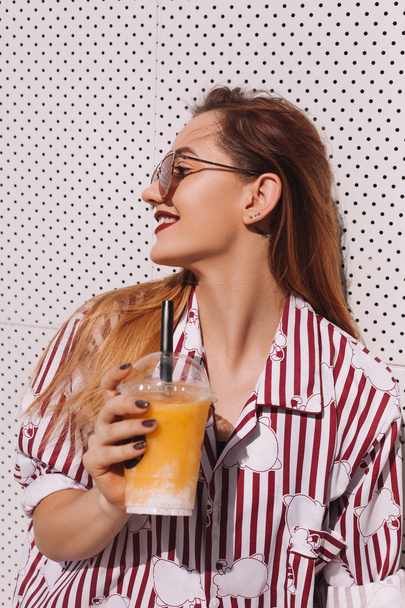 sensual woman with plastic cup of refreshing cocktail leaning back on white wall - Фото, зображення