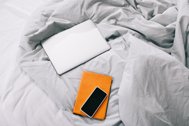 высокий угол обзора ноутбука с ноутбуком и смартфоном на одеяле в спальне
 - Фото, изображение