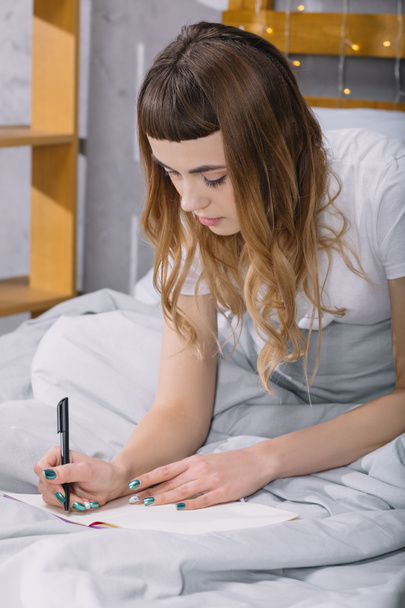 το κορίτσι γράφει κάτι στο σημειωματάριο στο κρεβάτι πρωί - Φωτογραφία, εικόνα