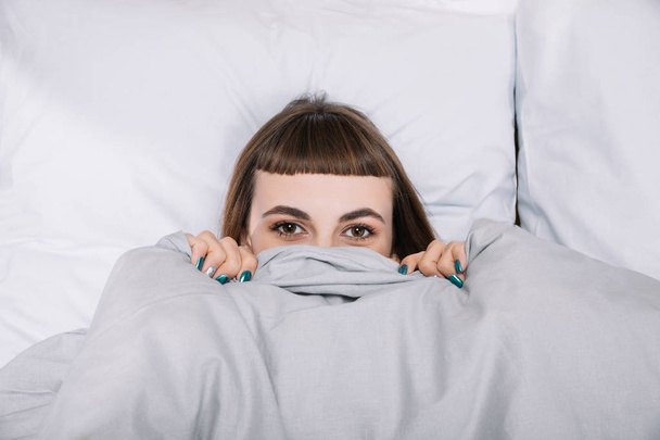 girl looking out from blanket in bedroom - Foto, Imagen