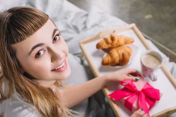 overhead view of happy girl holding gift box in bed - Fotó, kép