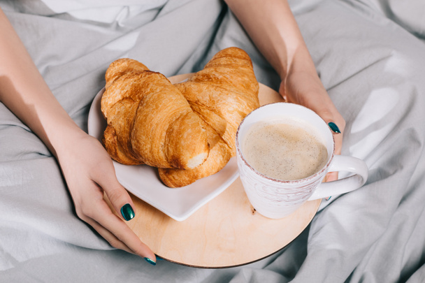 bijgesneden afbeelding van meisje houden dienblad met croissants en koffie - Foto, afbeelding