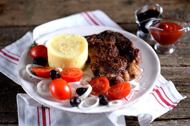 Яловичий стейк з картопляним пюре та салатом з вишневих помідорів, сушеними оливками та білою цибулею
. - Фото, зображення