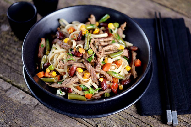Rice noodles with fried beef, corn, green peas, red and green carrots, parsley and spicy sauce. - Photo, Image