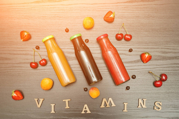 drei Flaschen mit Saft, Obst und Inschrift Vitamine auf schwarzem Holzgrund, Lebensmittelkonzept - Foto, Bild