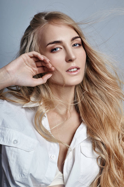 Mysterious and romantic with long blonde hair waving in the wind. Woman in the white shirt, beautiful eyes and clear skin. Sensual girl look, dynamic hair. - Foto, Imagem