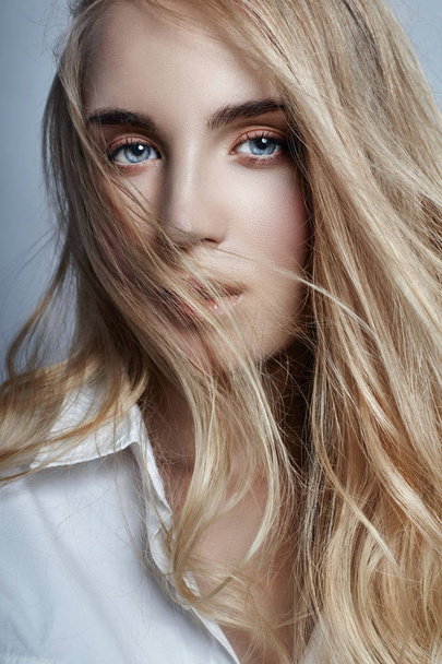 Mysterious and romantic with long blonde hair waving in the wind. Woman in the white shirt, beautiful eyes and clear skin. Sensual girl look, dynamic hair. - 写真・画像