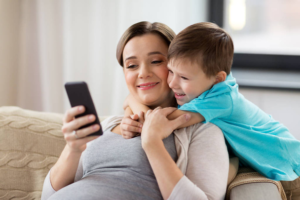 pregnant mother and son with smartphone at home - Foto, afbeelding