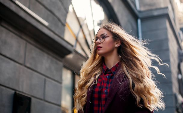 The concept of street fashion. Young beautiful model in the city. Beautiful blond woman wearing sunglasses. Hair fluttering in the wind. - Photo, Image