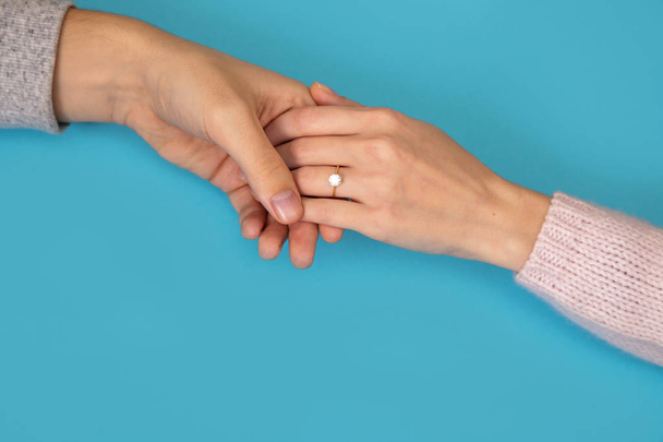 Ο άνθρωπος κάνει μια πρόταση να παντρευτεί τη φίλη του. Ανδρικά χέρια Βάλτε ένα δαχτυλίδι στο χέρι κορίτσια. Αρσενικό και θηλυκό τα χέρια με ένα δαχτυλίδι σε μπλε φόντο. - Φωτογραφία, εικόνα