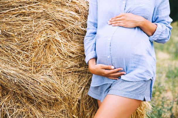 Donna incinta tiene le mani sulla pancia sullo sfondo della natura
 - Foto, immagini