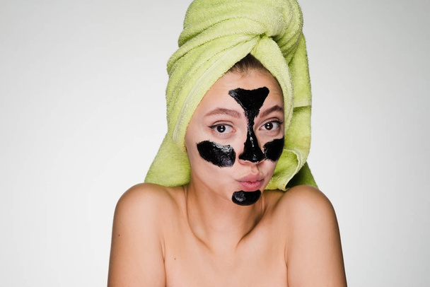 lovely funny girl with a green towel on her head applied a black cleansing mask to the problem areas on her face - Zdjęcie, obraz