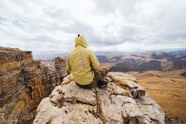 a male traveler sits on the edge of a cliff, enjoys the mountain nature - Фото, изображение