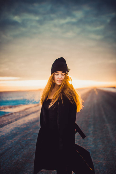 fashion woman in black clothes and hat on winter frozen road outdoor at sunset - Valokuva, kuva