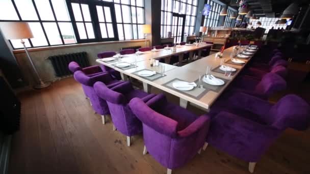 Πίνακες με γυαλιά και πιατάκια και μοβ πολυθρόνες στο εστιατόριο με μεγάλα παράθυρα - Πλάνα, βίντεο