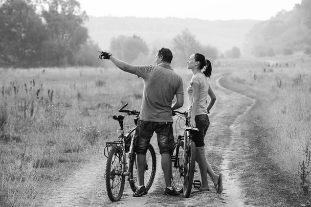 若いカップル、フィールドに自転車で。黒と白。ヨーロッパの人々. - 写真・画像