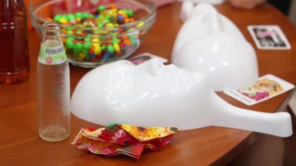 Masks, candies, bottle are on table and three people out of focus - Filmati, video