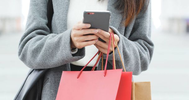 Donna shopping in possesso di sacchetti di carta e utilizzando il telefono cellulare
  - Foto, immagini