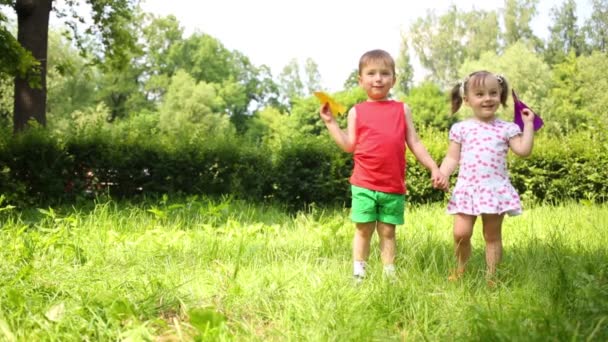 Kis boldog lány és egy fiú dobja papír repülőgépek park - Felvétel, videó