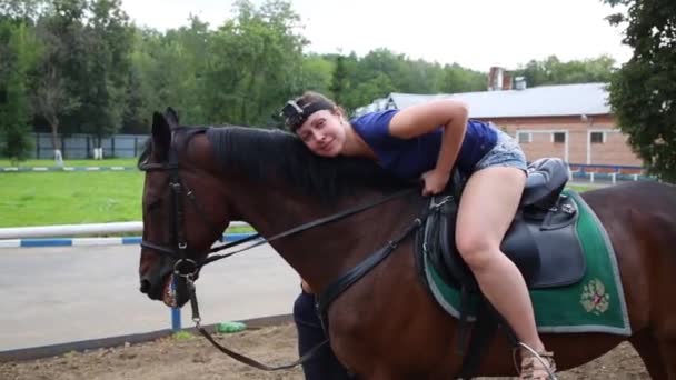 Smiling woman in shorts lies on horse with emblem on seat - Footage, Video