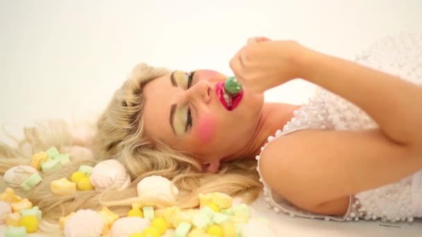 Smiling woman lies among sweets and sucks lollipop on floor - Footage, Video