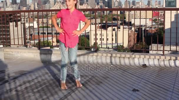 Little girl spins jumping at one place on roof against blue sky. - Séquence, vidéo