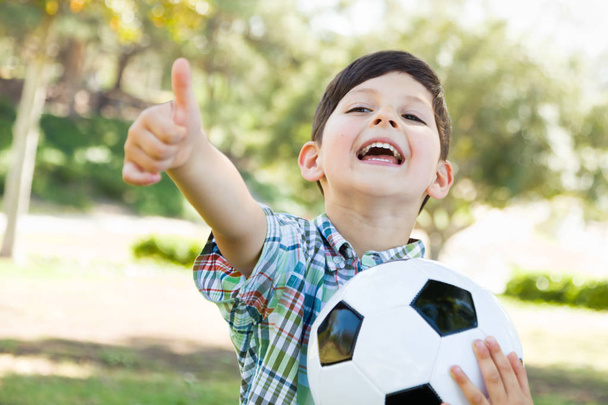 Roztomilý mladý chlapec hrát s fotbalovým míčem a palce venku v parku. - Fotografie, Obrázek