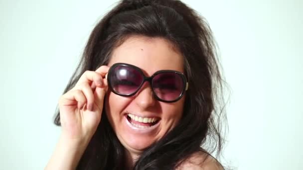 Dark-haired laughing girl model in dark sunglasses poses at studio. - Záběry, video
