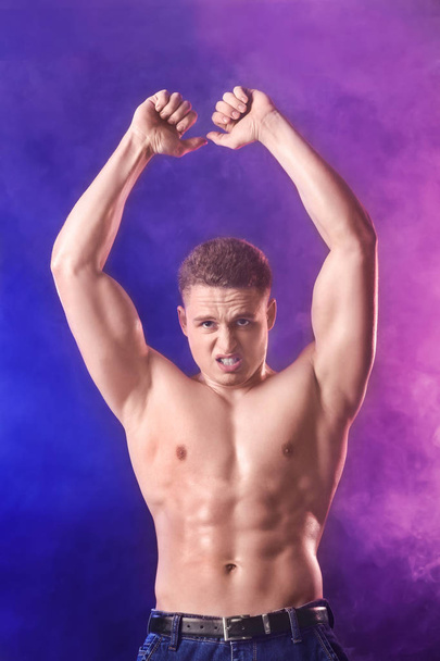 Muscular young bodybuilder in colorful smoke - Foto, afbeelding