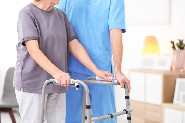Senior woman walking with assistance of young caregiver indoors - Foto, Imagen