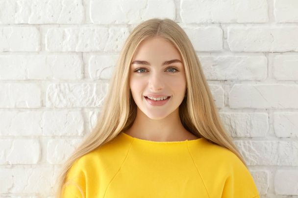 Smiling woman in yellow sweatshirt on brick wall background - Foto, Imagen