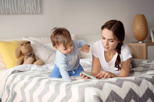 Beautiful young woman reading to her baby on bed at home - Foto, Imagem