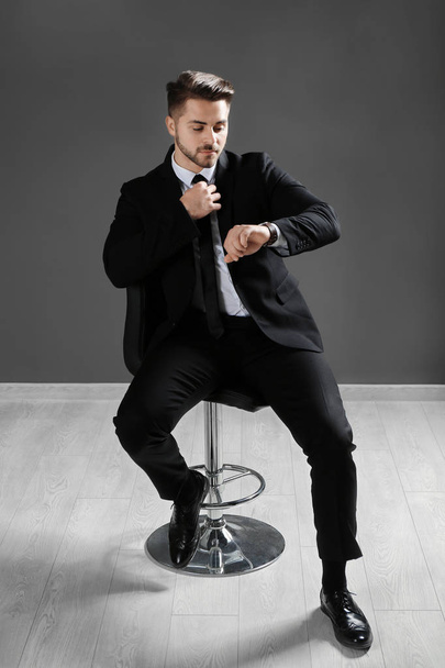 Handsome man in formal suit sitting on chair against grey wall - 写真・画像