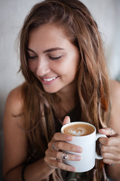 portrait of beautiful smiling girl is holding cup of coffe with heart form foam - Photo, image