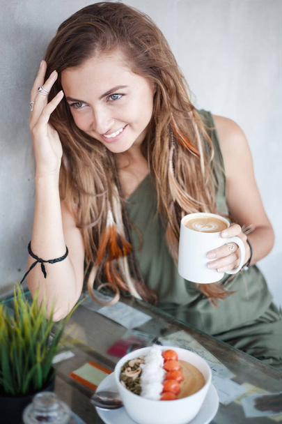 Beautiful smiling girl with cup of coffee and muesli bowl is sitting in a cafe - 写真・画像