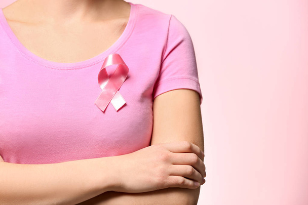 Woman with pink ribbon on t-shirt against color background. Breast cancer awareness concept - Foto, Imagen
