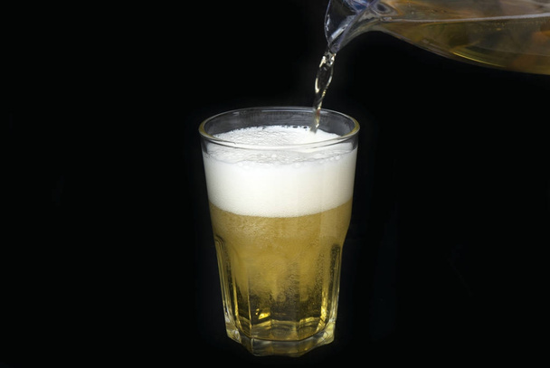 Поток пива в стакане на черном фоне
. - Фото, изображение