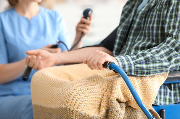 Young caregiver measuring blood pressure of senior man at home - Fotografie, Obrázek