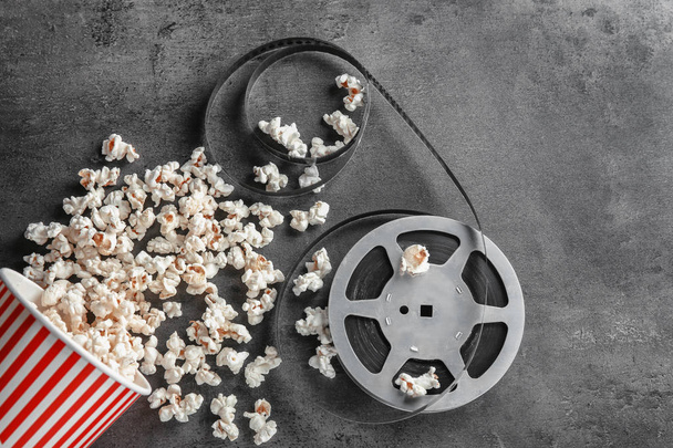 Paper cup with tasty popcorn and movie reel on grey background - Фото, зображення